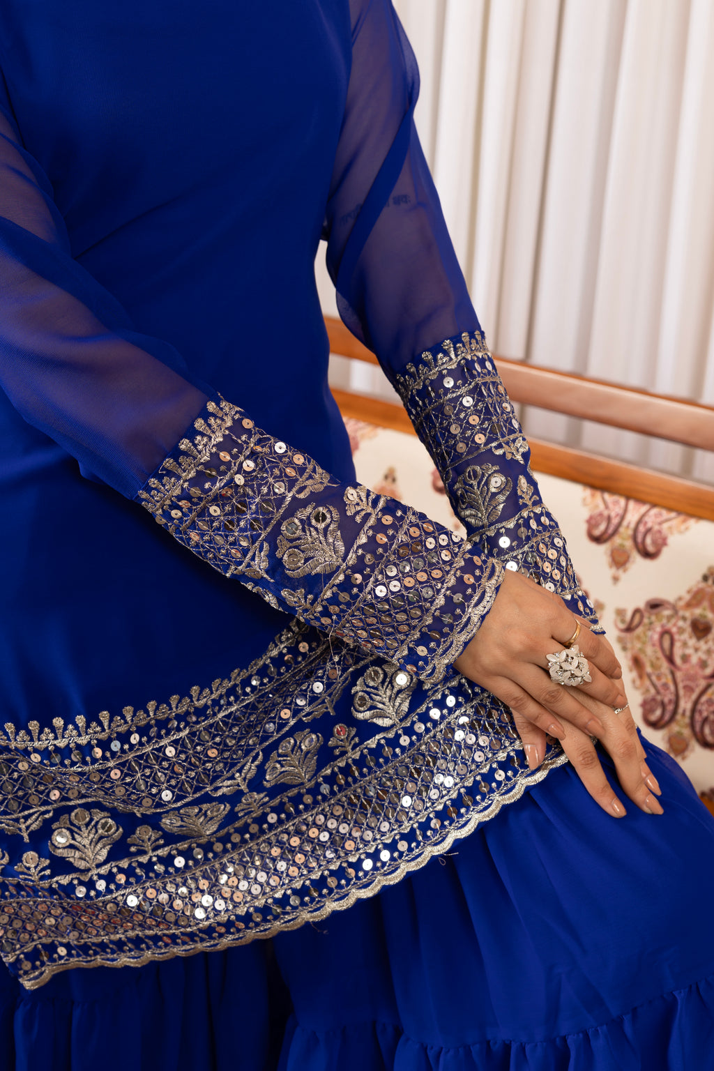 Blue embroidered garment with intricate patterns on a patterned chair.