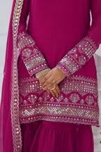 Close-up of a magenta traditional outfit with intricate gold embroidery.