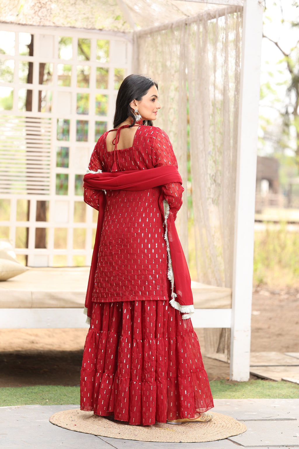 Person wearing a red dress with white patterns, standing on a wooden platform.