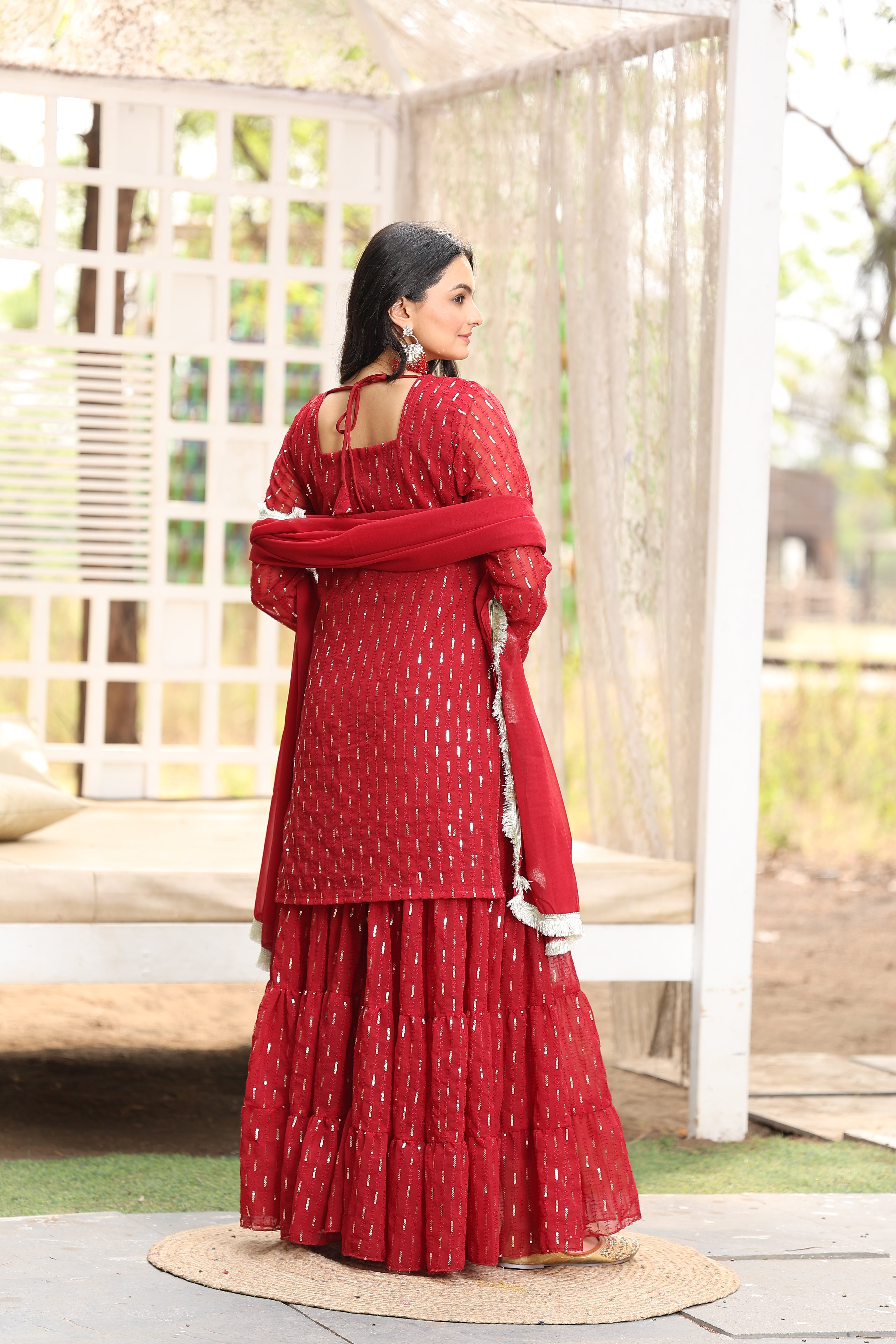 Person wearing a red dress with white patterns, standing on a wooden platform.