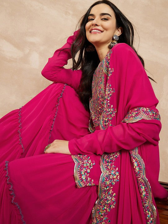 Woman in a bright pink traditional outfit with intricate embroidery on a beige background