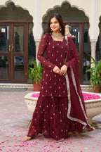 Woman in a maroon traditional outfit standing in front of a decorative building entrance.