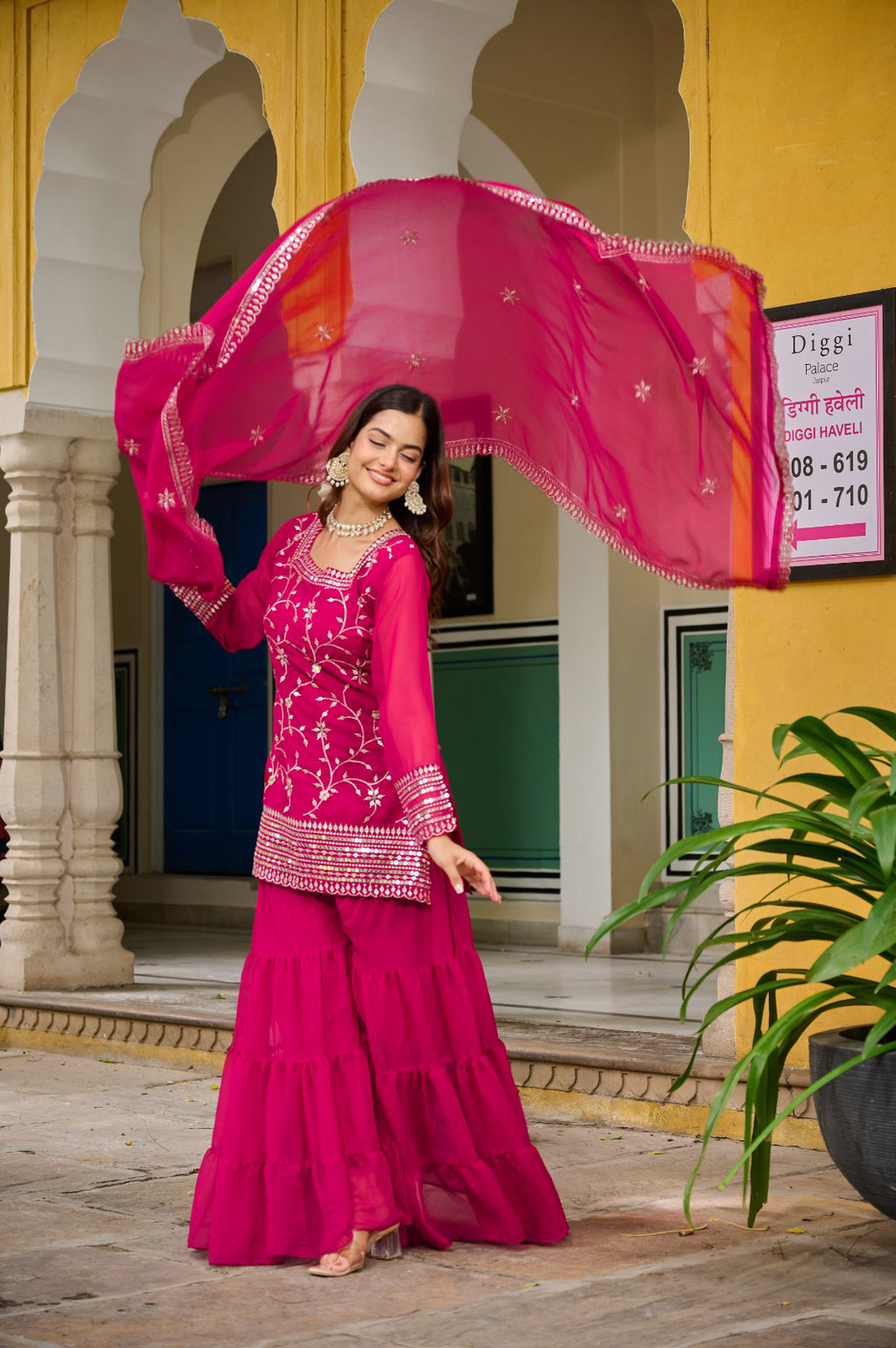 Woman in a pink dress standing in front of a yellow building with arches.