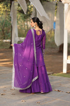 Woman in a purple traditional outfit standing outdoors on a paved path.