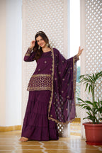 Woman in a purple traditional outfit with gold details standing indoors.