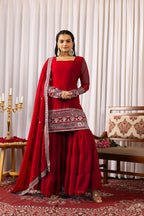 Woman in a red traditional outfit with intricate patterns in a decorated room.