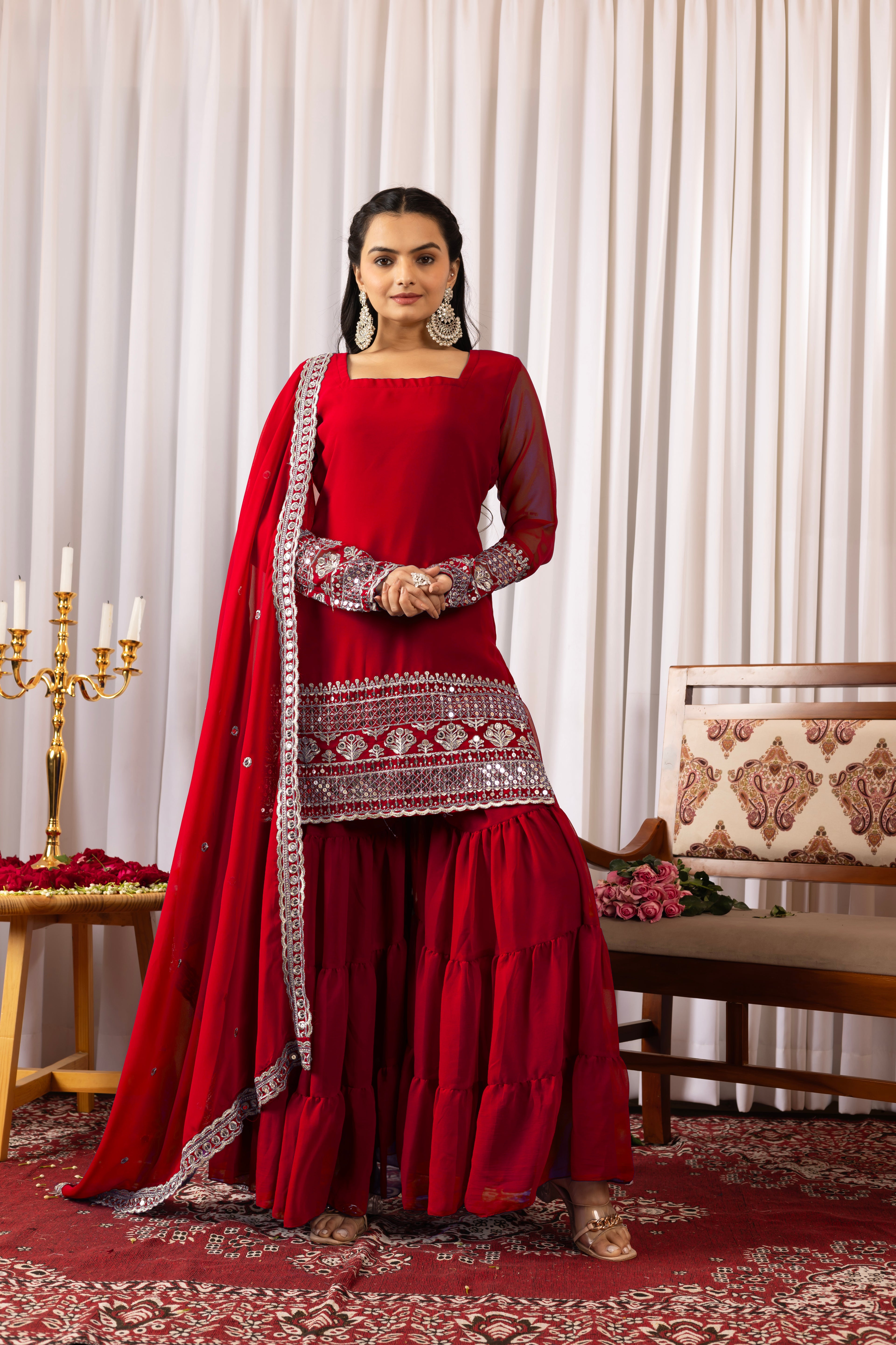Woman in a red traditional outfit with intricate patterns in a decorated room.