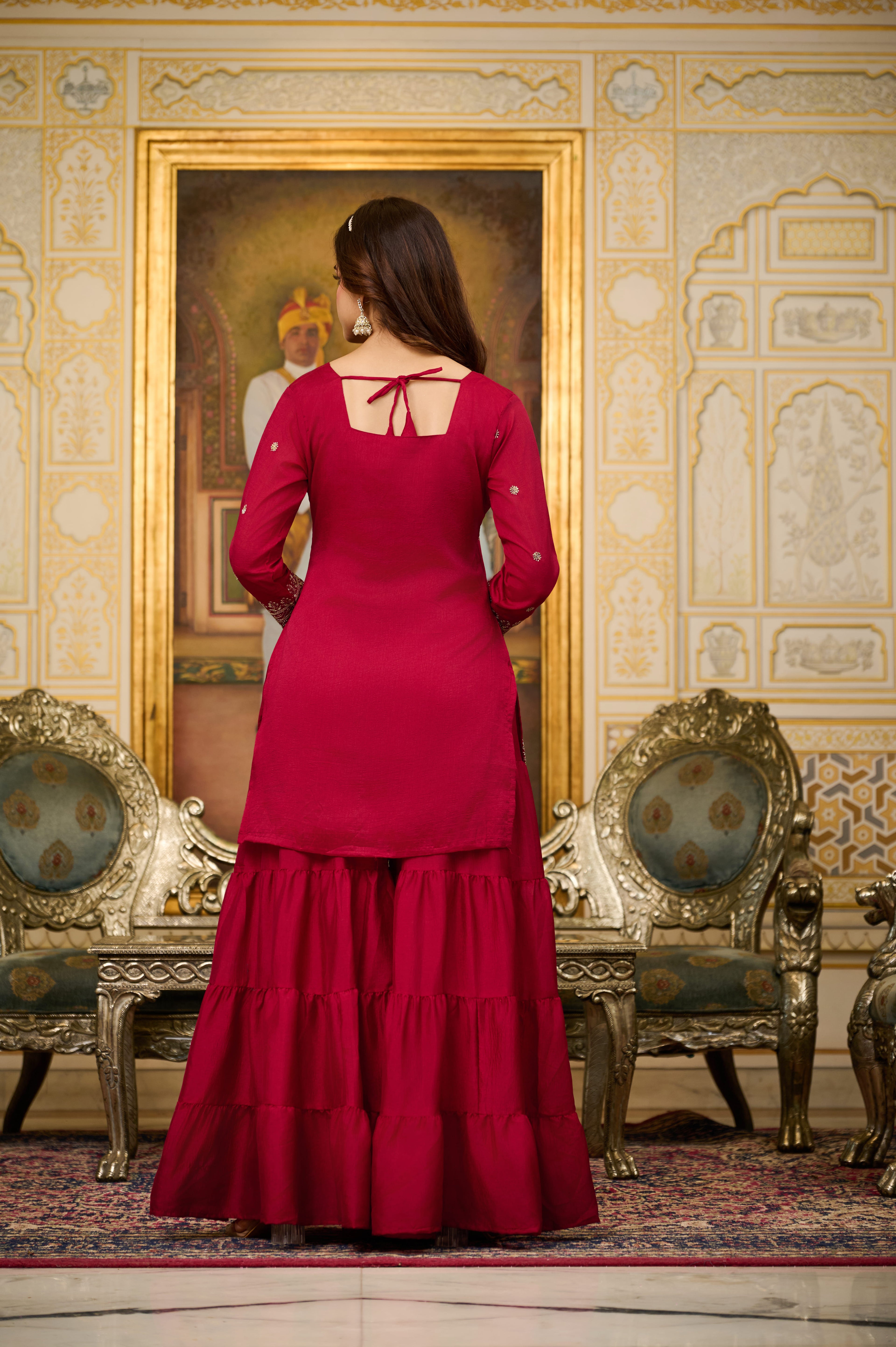 Woman in a red dress standing in an ornate room with decorative walls and furniture.