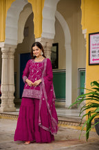 Woman in a vibrant pink traditional outfit standing in front of a building with arches.