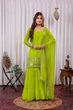 Woman wearing a bright green traditional outfit with embroidery in a decorated indoor setting.