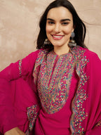 Woman wearing a bright pink traditional outfit with intricate embroidery against a beige background