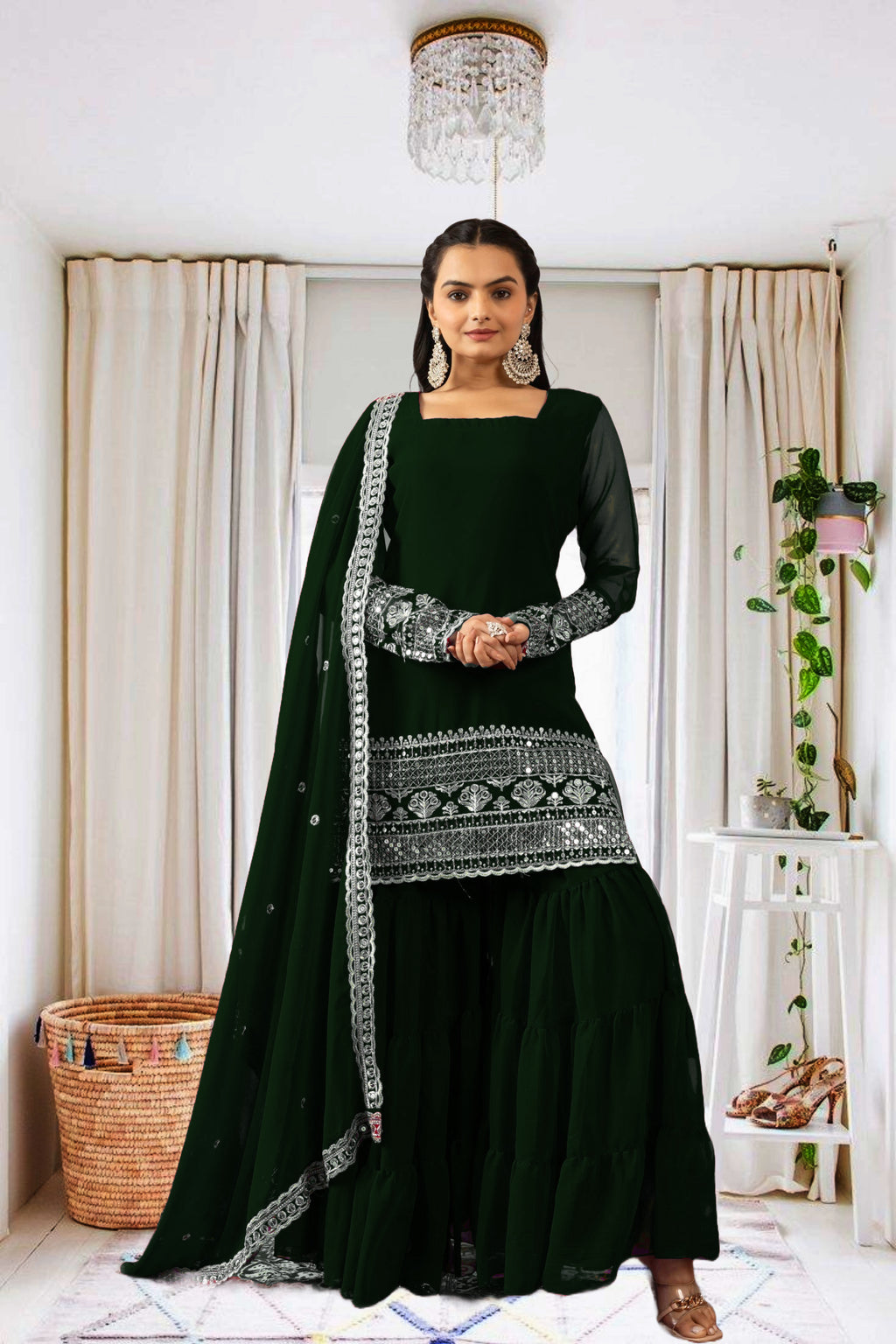 Woman wearing a dark green traditional outfit with silver embroidery in a home setting.