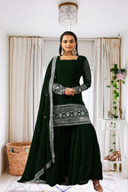 Woman wearing a dark green traditional outfit with silver embroidery in a home setting.