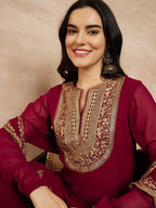 Woman wearing a maroon traditional outfit with gold embroidery on a beige background