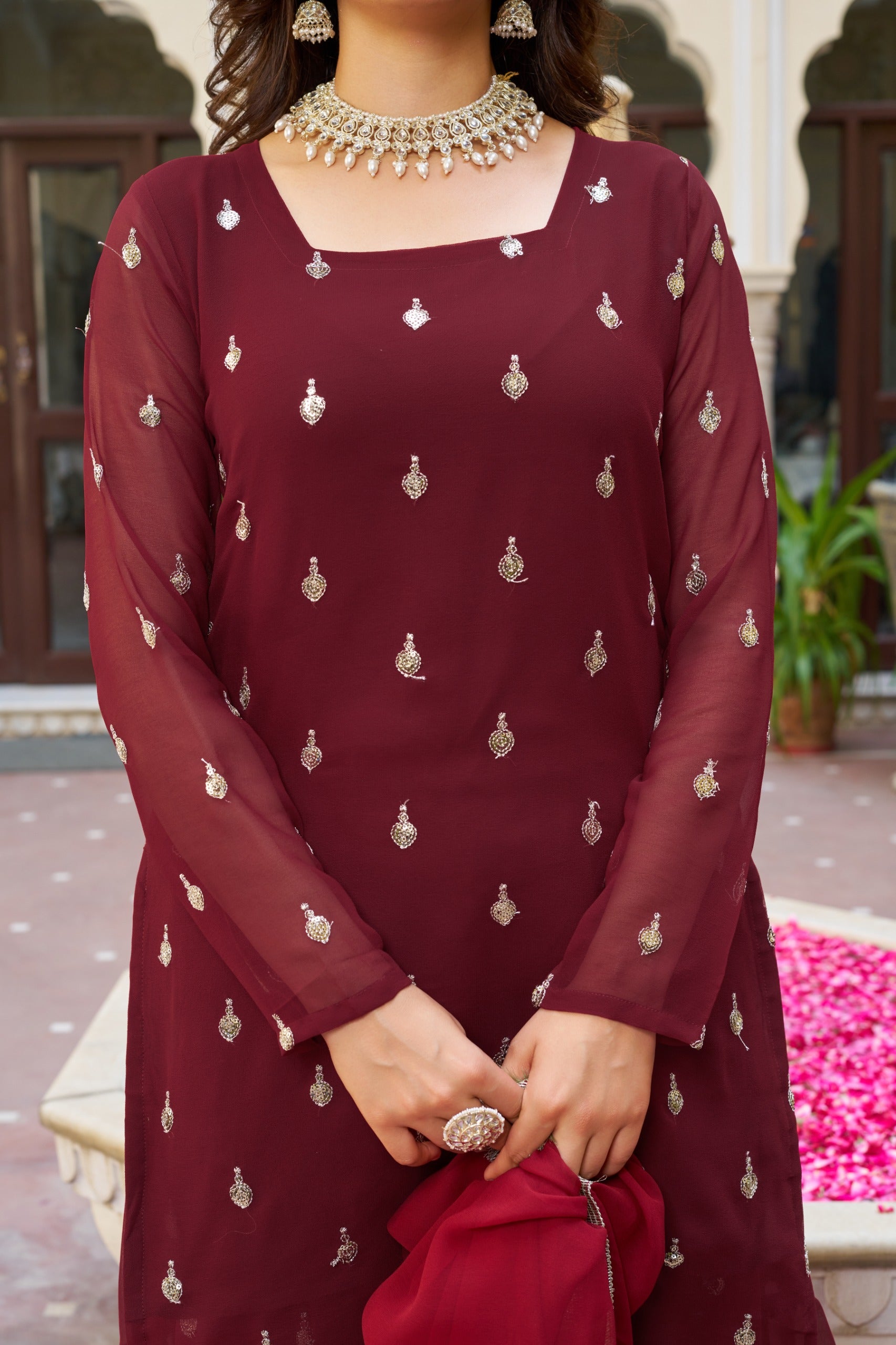 Woman wearing a maroon dress with intricate patterns, standing outdoors.