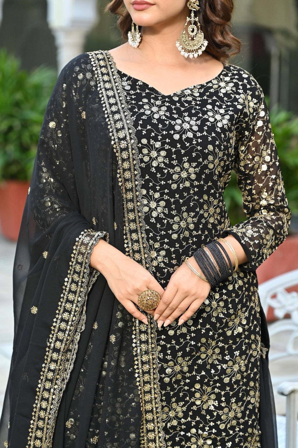 Woman wearing a black and gold embroidered traditional outfit with a dupatta.