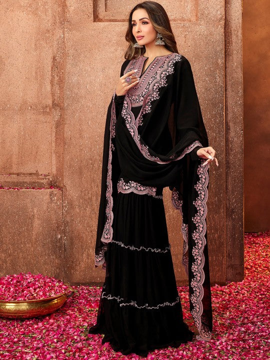 Woman in a black and purple traditional outfit standing on pink petals with a decorative background.