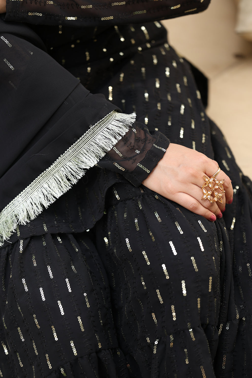 Person wearing a black outfit with gold patterns, holding a small decorative item.