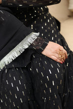 Person wearing a black outfit with gold patterns, holding a small decorative item.