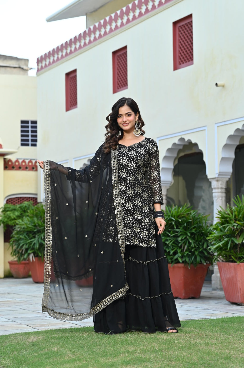 Woman in a black traditional outfit standing in front of a building with plants.
