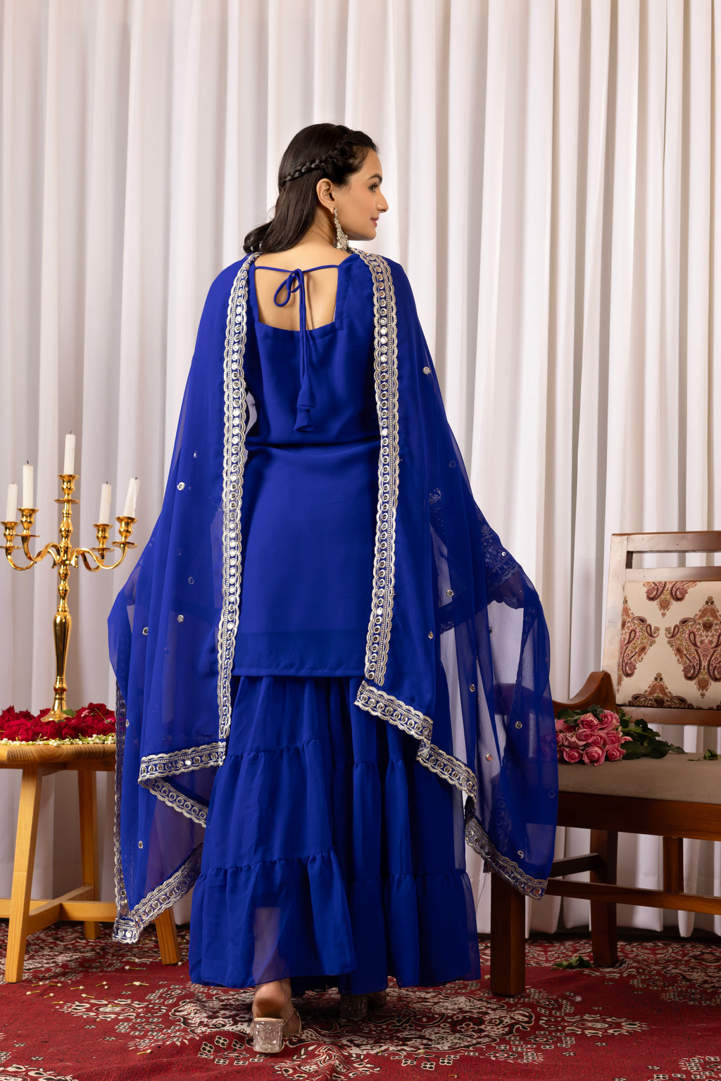 Woman in a blue traditional outfit with silver detailing in a decorated room.