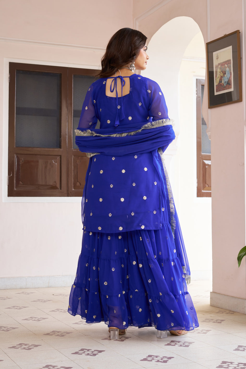 Woman wearing a blue traditional outfit with white patterns in a room.