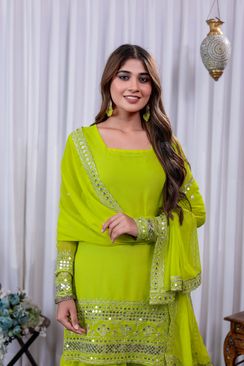 Woman wearing a bright green traditional outfit with embroidery against a white curtain background