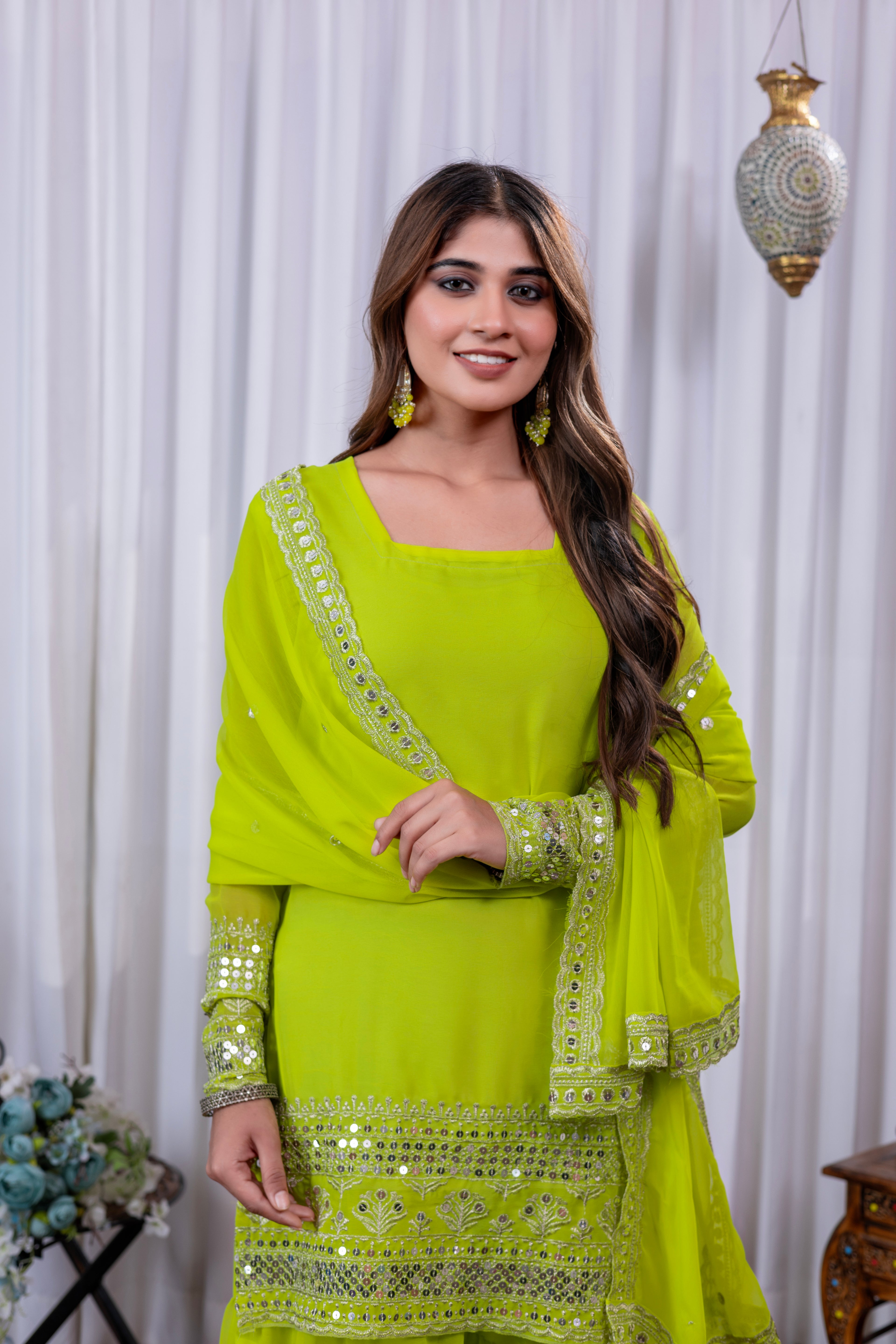 Woman wearing a bright green traditional outfit with embroidery against a white curtain background