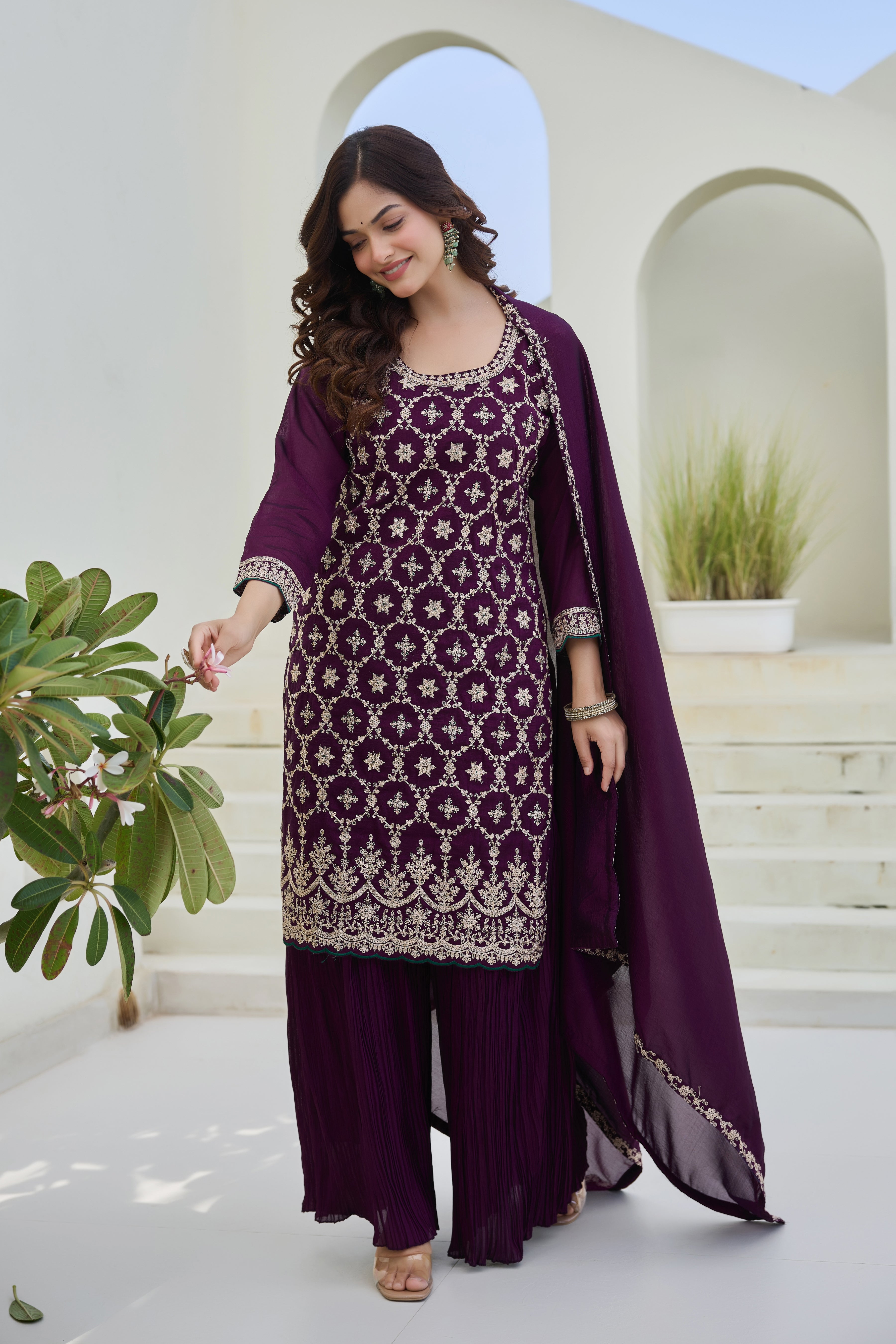 Woman in a purple traditional outfit with a matching dupatta standing in a bright outdoor setting.