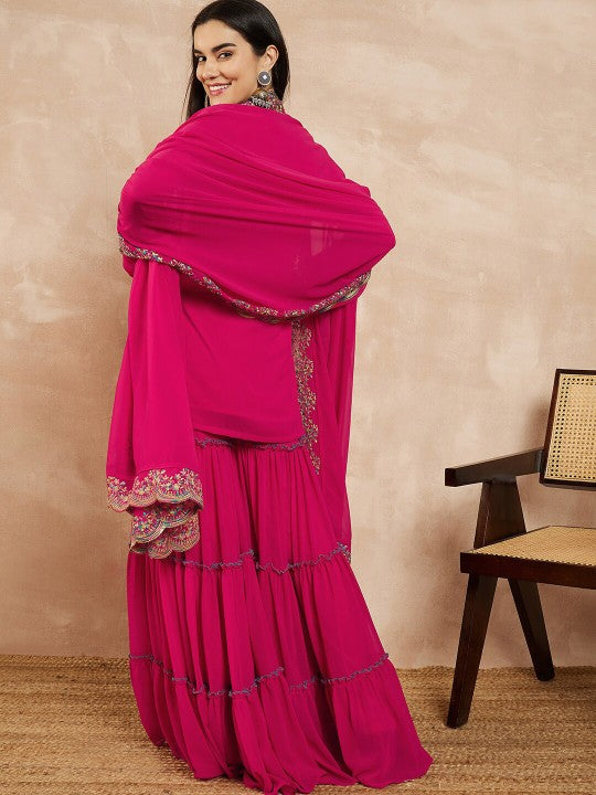 Woman wearing a bright pink traditional outfit with a matching dupatta on a beige background