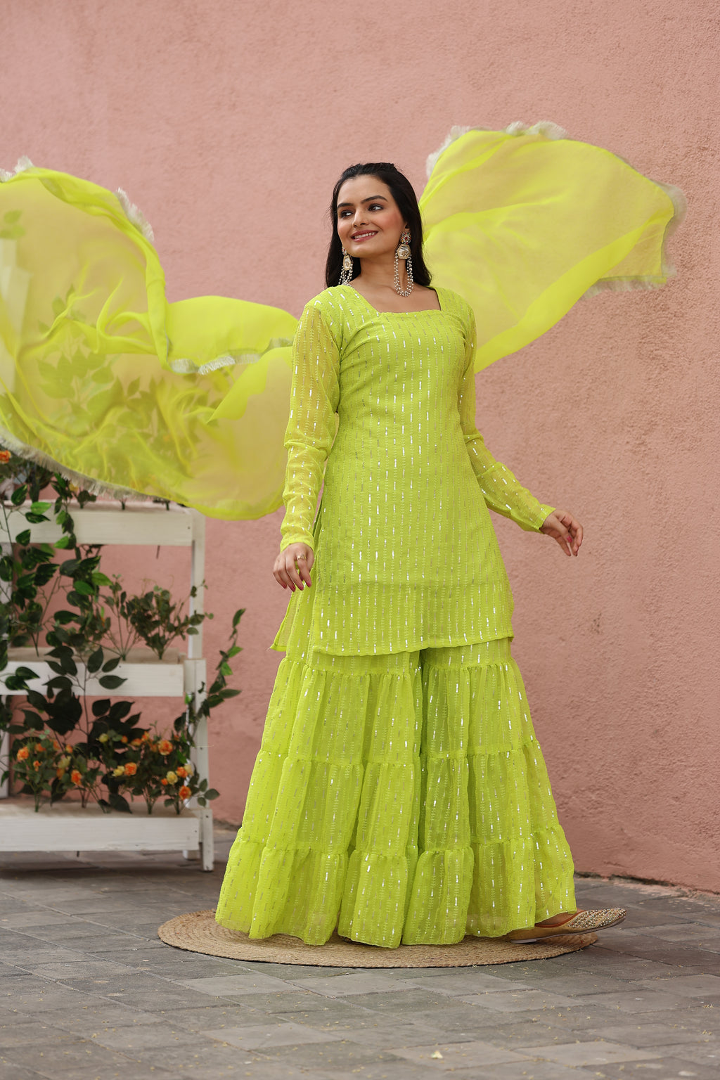 Woman in a bright yellow dress standing against a pink wall with plants.