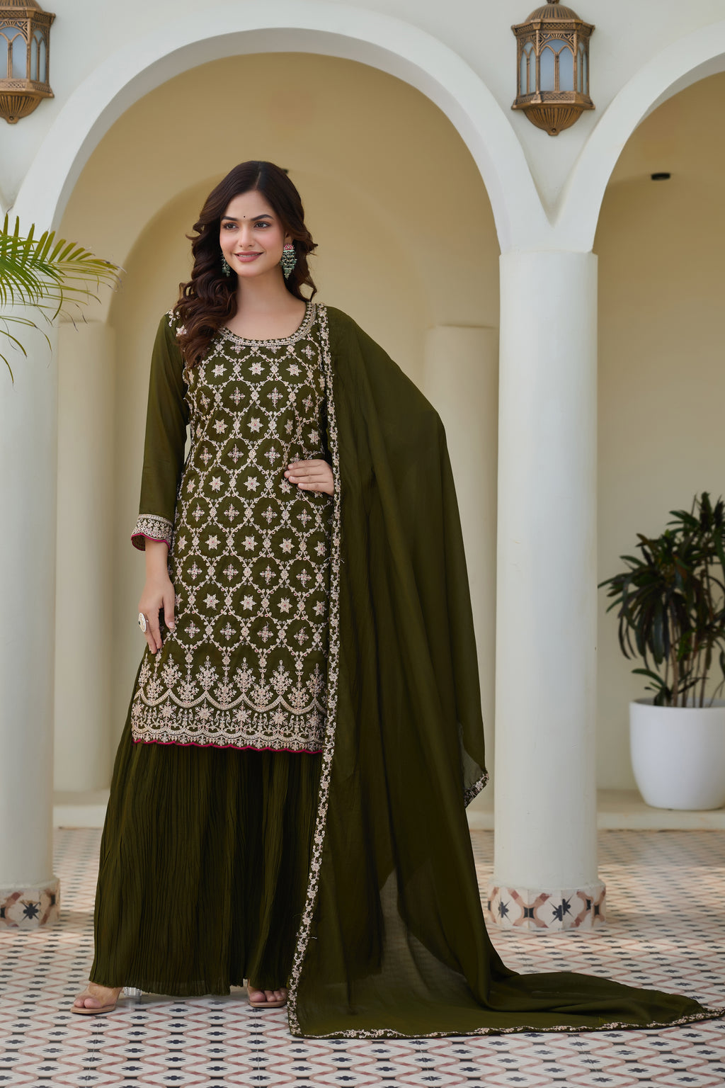 Woman in a green traditional outfit with embroidery standing in an archway.