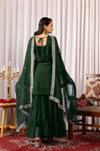 Woman in a dark green traditional outfit with a matching dupatta in a decorated room.