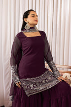 Woman in a dark purple traditional outfit with silver embroidery against a white curtain background