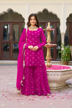 Woman in a pink traditional outfit standing in front of a decorative fountain with pink petals on the ground.