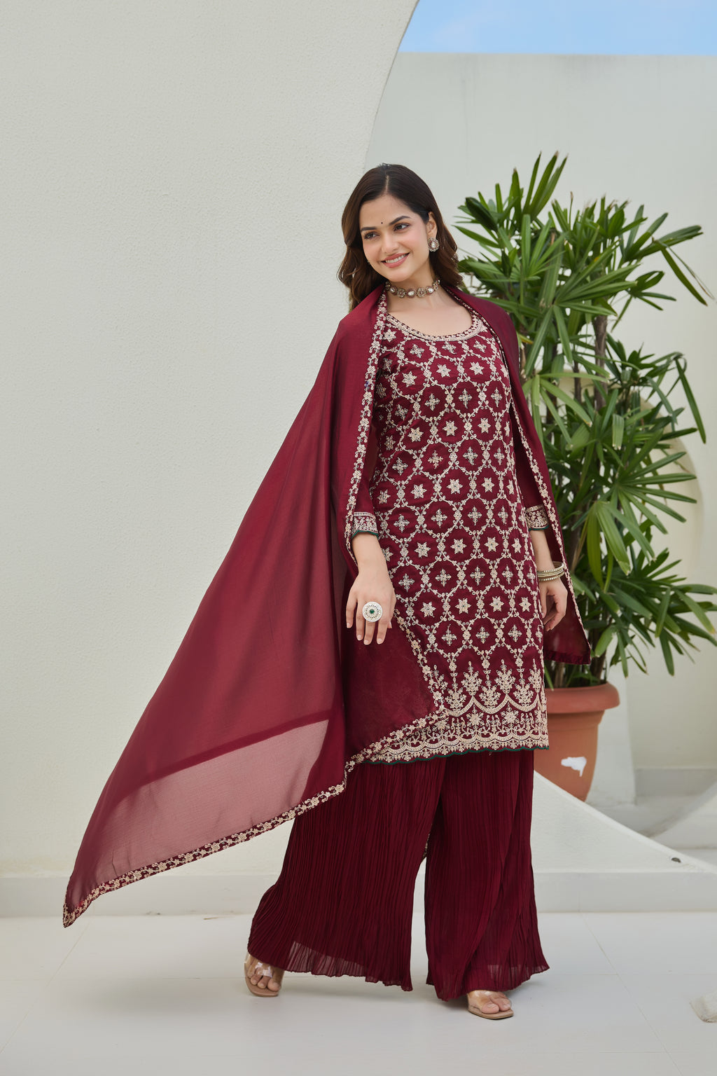 Woman in a maroon traditional outfit with a plant in the background