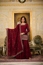 Woman in a red traditional outfit standing in an ornate room with decorative walls and furniture.