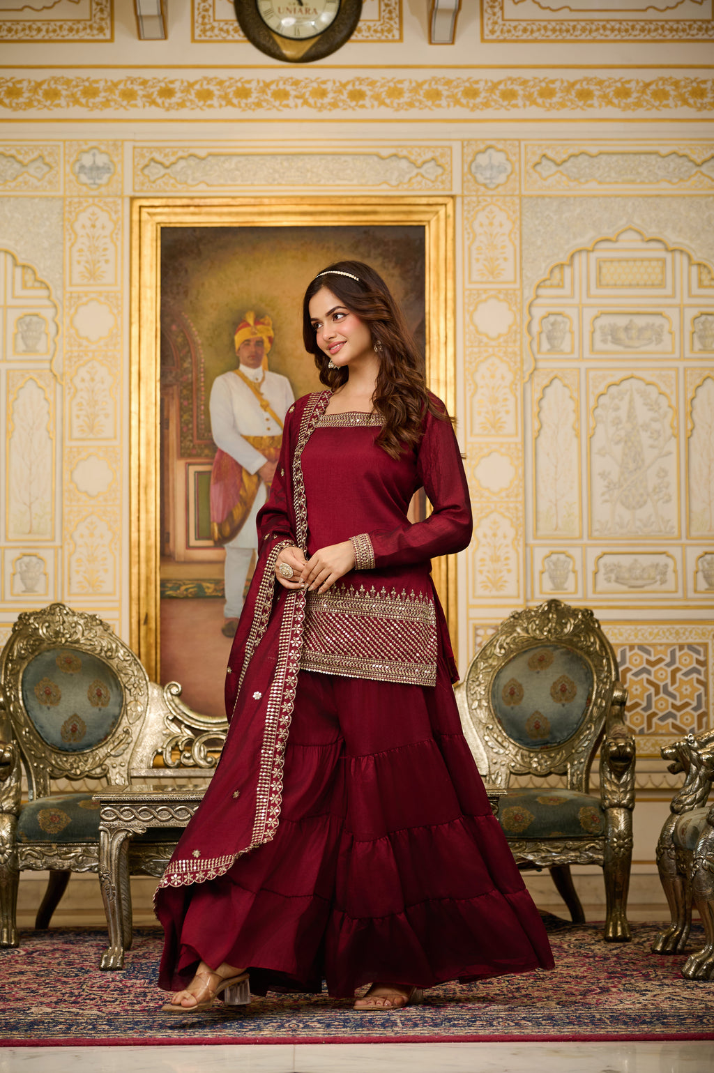 Woman in a red traditional outfit standing in an ornate room with decorative walls and furniture.