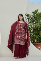 Woman wearing a maroon traditional outfit with white patterns against a neutral background