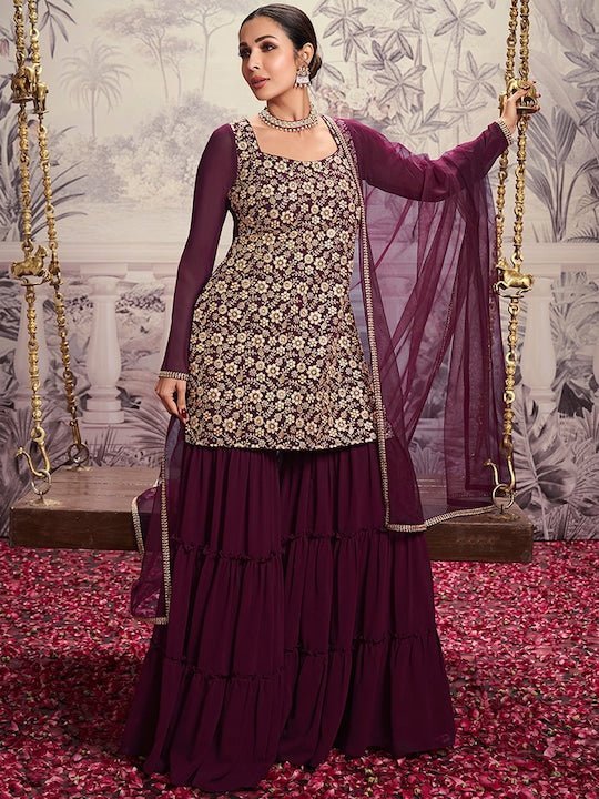 Woman in a traditional outfit with a floral top and purple sharara on a swing.