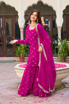 Woman in a pink traditional outfit standing in front of an architectural building with plants.