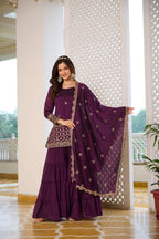 Woman in a purple traditional outfit with gold details standing indoors.