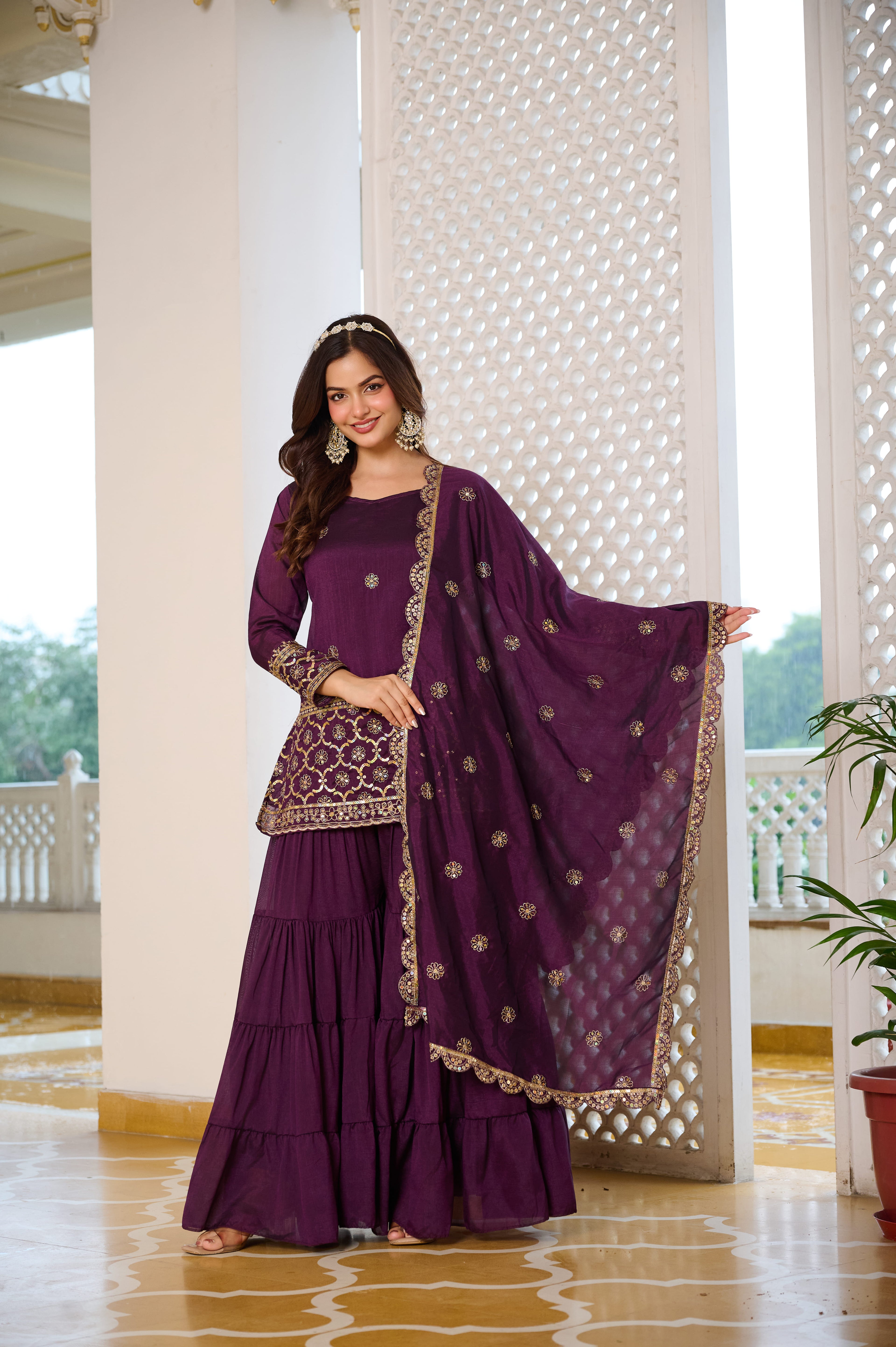 Woman in a purple traditional outfit with gold details standing indoors.