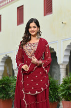 Woman in a red traditional outfit with intricate patterns standing in front of a building.