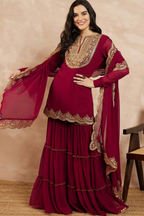 Woman wearing a maroon traditional outfit with gold embroidery against a beige background