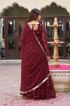 Woman in a maroon dress with gold border standing in front of a decorative fountain.