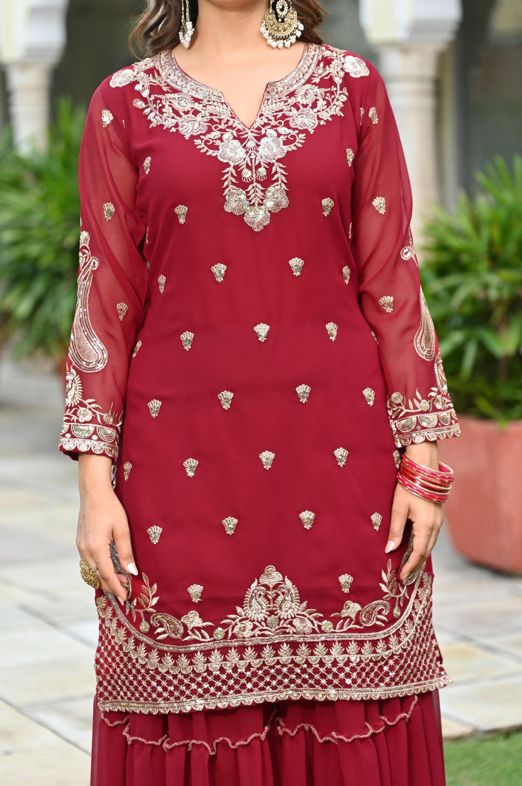 maroon embroidered traditional outfit with gold details worn by a person outdoors.