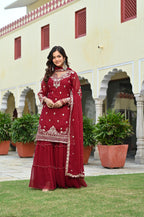 Woman in a maroon traditional outfit standing in front of a building with plants.