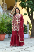 Woman in a red and gold traditional outfit standing outdoors with plants and a staircase in the background.