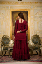 Woman in a red traditional outfit standing in a decorated room with ornate walls and furniture.